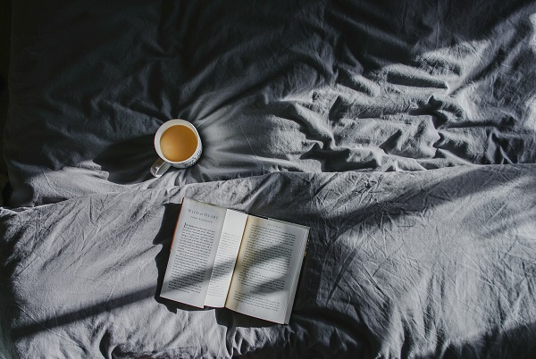 an open book and cup of coffee lie on a bed. Some library books can still be check out and picked up at the curb