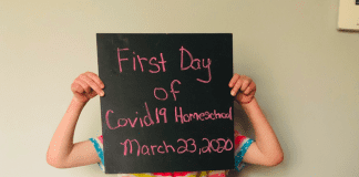 A child holds up a sign saying 'first day of covid19 homeschooling'
