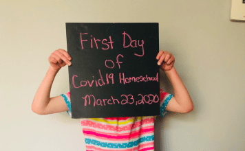 A child holds up a sign saying 'first day of covid19 homeschooling'
