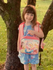 Young girl in front of tree with lunchbox