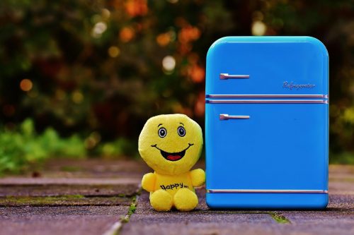 Photo of small blue refrigerator with a yellow stuffed smiley face next to it