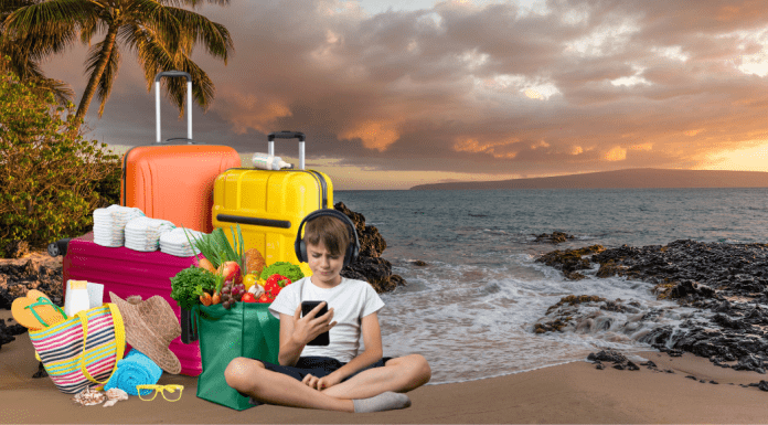 Background: beach at sunset. Foreground: suitcases, grocery bags sit on the sand, while a kid with headphones on stares at a cell phone.